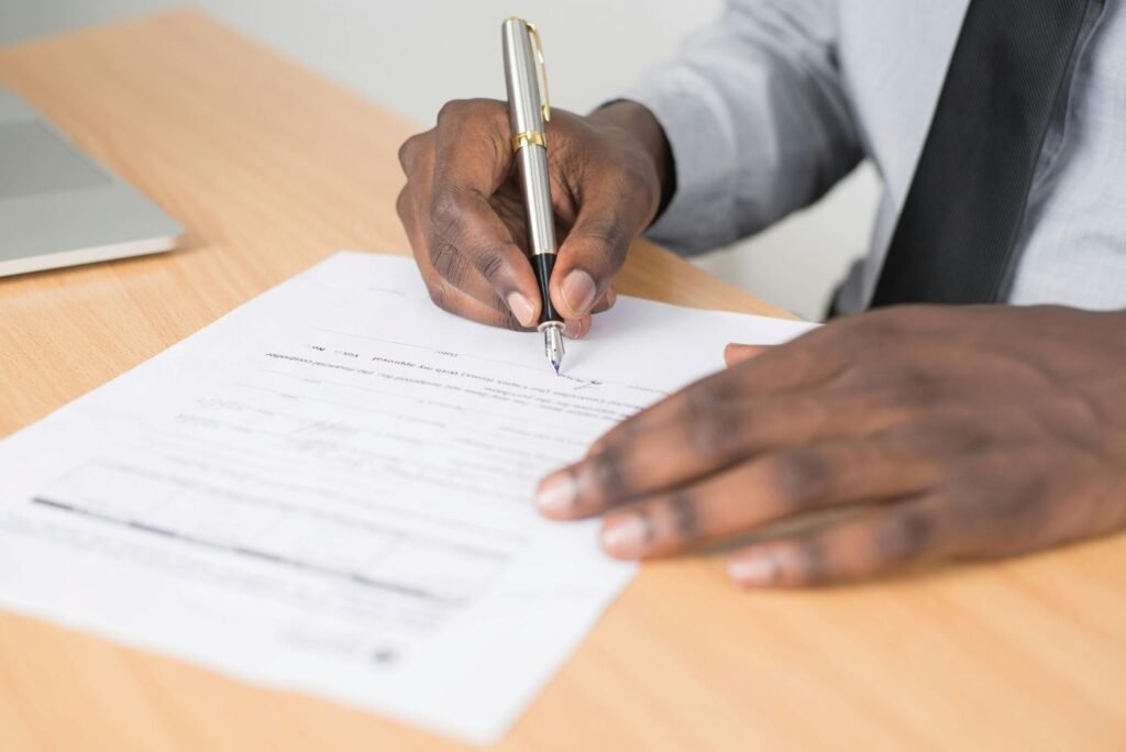 Close-up image of a person signing the necessary paperwork for NRE Nomination for NRIs/OCIs on a wooden desk.